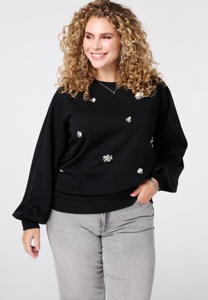 Zwarte sweatshirt met lange, geblazen mouwen en florale versieringen. Zacht materiaal, relaxte pasvorm, geribbelde zoom, gecombineerd met lichtgrijze jeans.