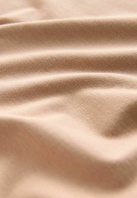 Mäkká béžová látka s jemnou textúrou, zobrazená v zábere zblízka s jemnými záhybmi a slabými tieňmi vytvárajúcimi hĺbku.