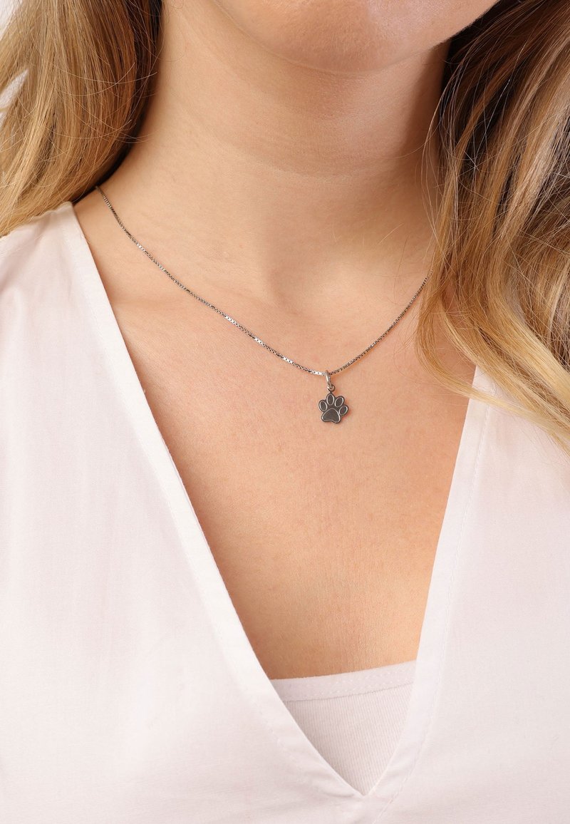 Zilveren ketting met een hangertje in de vorm van een pootafdruk op een lichte achtergrond, met een delicate vormgeving en een gladde textuur.