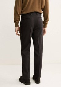 Pantaloni tailored marroni scuri con vestibilità dritta, dotati di due tasche posteriori e una texture liscia, indossati con un maglione marrone chiaro.