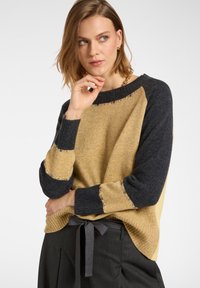 Sweter dzianinowy z musztardowym przodem, ciemnoszarymi rękawami i zdobieniami na dekolcie oraz mankietach. Miękka tekstura, luźny krój.