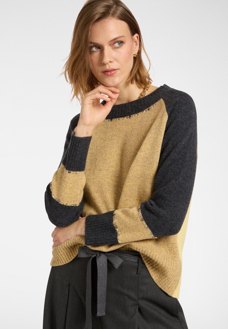 Sweter dzianinowy z musztardowym przodem, ciemnoszarymi rękawami i zdobieniami na dekolcie oraz mankietach. Miękka tekstura, luźny krój.
