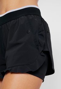 Svarta idrottsshorts med en volangkant, elastisk midja i svart med en ljusgrå accent, med en sidficka och mjuk textur.