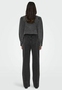 Chaqueta de mezclilla negra con mangas abullonadas y jeans rectos de cintura alta a juego. Ambos tienen costuras visibles y bolsillos traseros sutiles.