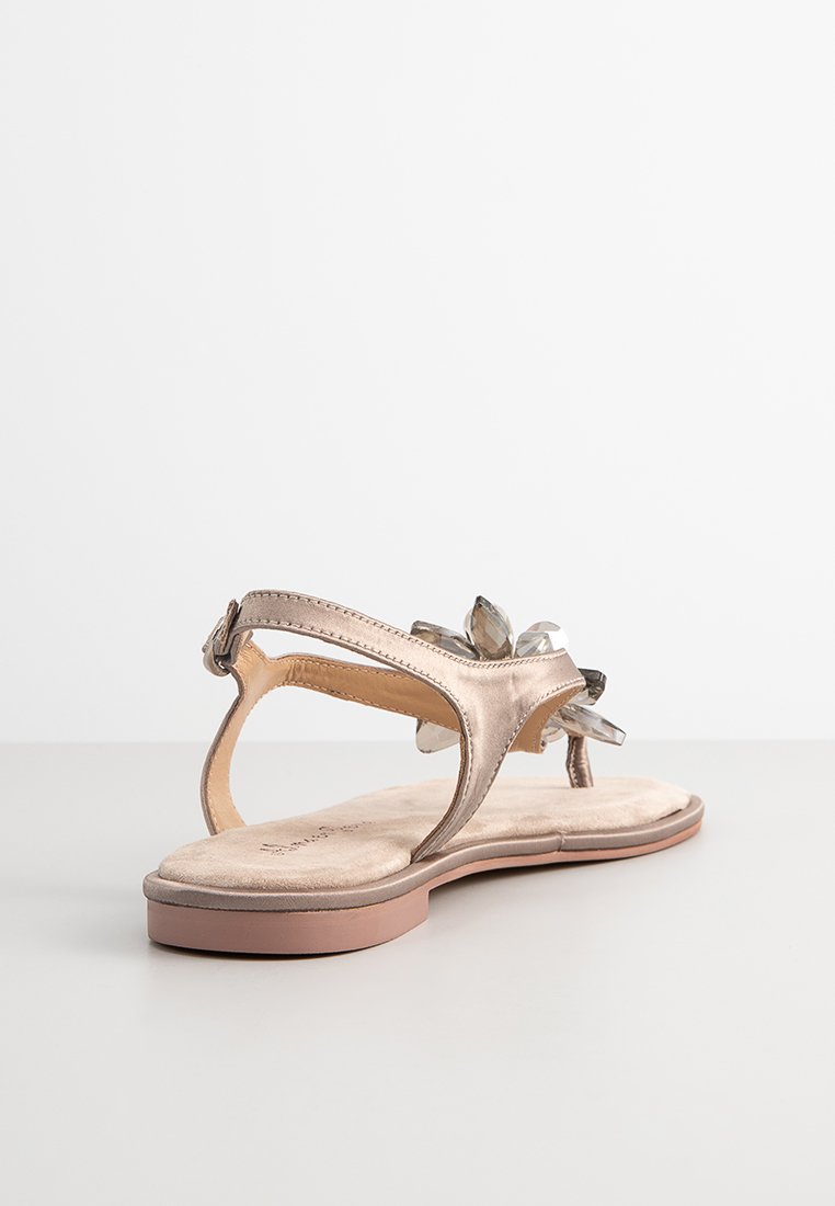 Metallisch goldene Sandale mit flacher Sohle, die ein florales Detail aus klaren Edelsteinen aufweist. Offene Ferse und verstellbarer Riemen für eine optimale Passform.