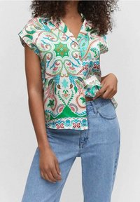Blusa de manga corta impresa en tela ligera, con un colorido patrón de paisley en tonos verdes, azules y rojos. Combinada con jeans de mezclilla.