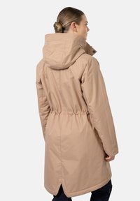 Beige lång jacka med huva, elastisk midja och slitsar på sidorna vid fållen. Tillverkad av ett slätt och hållbart material. Minimalistisk design.