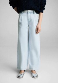 Jeans azzurri a palazzo con pieghe e vita alta; abbinati a ballerine argentate con un dettaglio a fiocco.