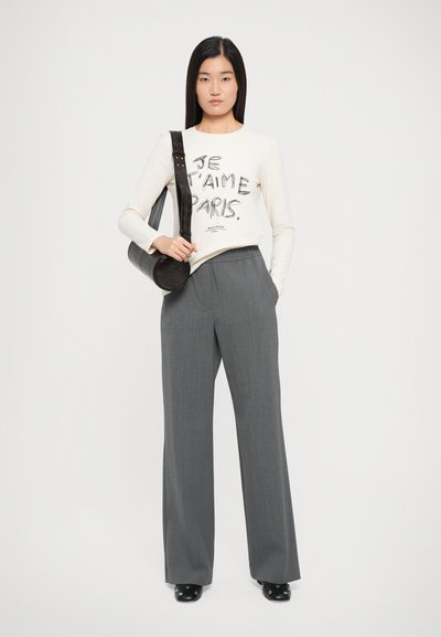 Lange mouw crème shirt met zwarte print met de tekst “JE T'AIME PARIS,” gecombineerd met grijze broek met wijde pijpen en een zwarte ronde tas.