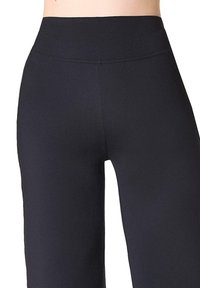 Czarne legginsy z wysokim stanem wykonane z gładkiego, elastycznego materiału, z bezszwowym designem i dopasowanym krojem sięgającym do kostek.