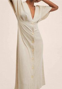 Robe beige clair avec un décolleté en V profond, des manches courtes, et un devant à boutons avec six boutons de couleur claire. Tissu lisse et coupe confortable.