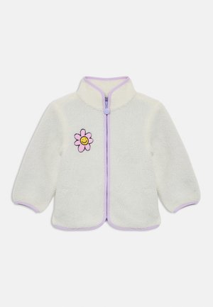 Casaco de felpa branco com um fecho roxo, apresentando um bordado de uma flor rosa e uma cara sorridente do lado esquerdo. Textura suave e bainha arredondada.