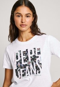 Bílá bavlněná tričko s barevným květinovým vzorem uvnitř textu "PEPE JEANS". Kulatý výstřih a krátké rukávy.