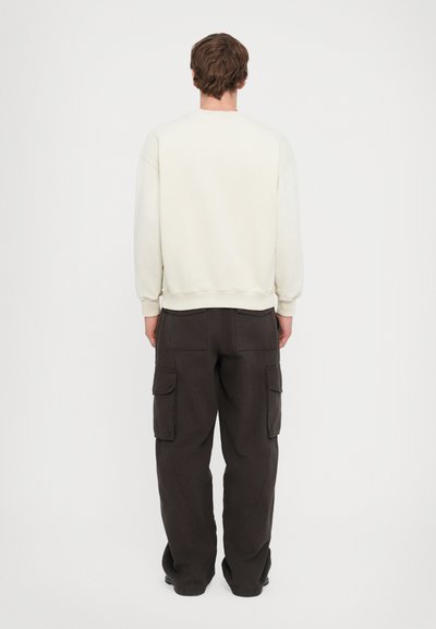 Lys beige sweatshirt med ribbede manchetter og kant, parret med mørke cargo bukser med sidelommer og en løs pasform.