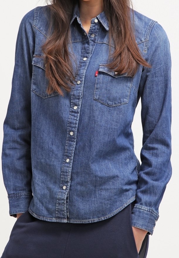 Chemise en denim à manches longues, couleur bleu clair, deux poches poitrine, et fermeture boutonnée devant. Dotée d'un col pointu et d'une légère courbe à l'ourlet.