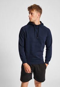 Helleblaues Hoodie mit Kängurutasche, verstellbaren Kordelzügen, gerippten Bündchen und Saum. Kombiniert mit schwarzen Shorts. Weicher Stoff.