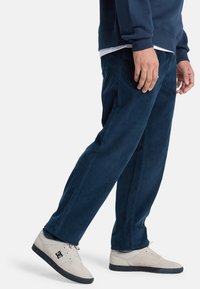 Marineblauwe corduroy broek met een rechte pasvorm, zijzakken en subtiele textuur, gecombineerd met lichte sneakers met een zwart logo.