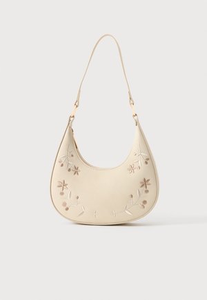 Sac à main en forme de croissant couleur crème avec une broderie florale et une courte sangle, suspendu sur un fond blanc.