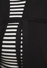 Black cardigan with a tied waist, layered over a black and white striped top. Features smooth textures and ribbed accents along the edges.