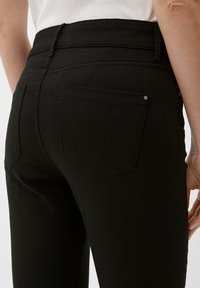 Jean noir taille haute avec une coupe ajustée, poches arrière plates et détails de couture subtils, fabriqué en tissu en coton extensible.
