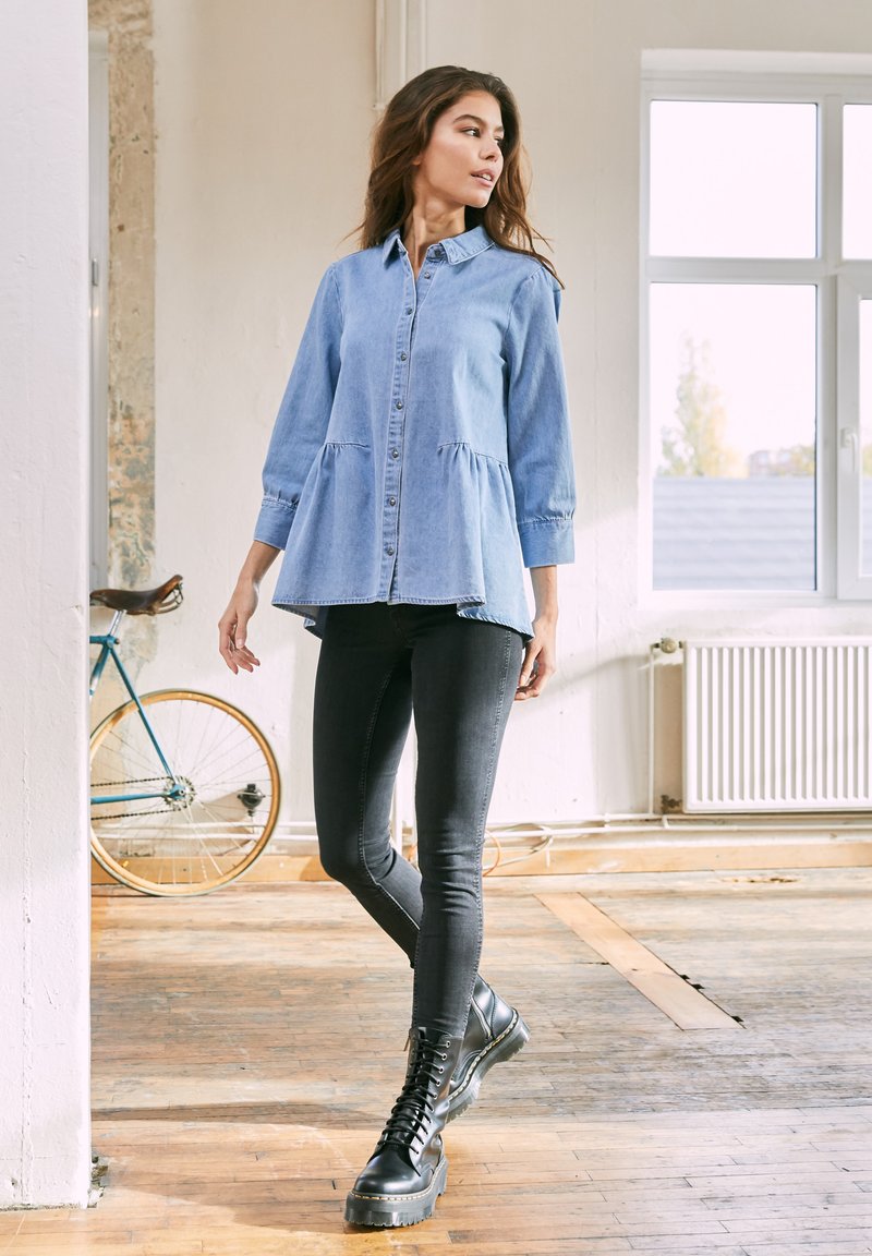 Light blue denim shirt with a flared hem, button closure, and long sleeves, paired with black skinny jeans and black lace-up ankle boots.