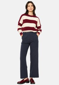 Chunky kastanjebruin en crème gestreepte trui met lange mouwen, gecombineerd met hooggehakte marineblauwe gestreepte broek en glanzende bordeauxrode loafers.