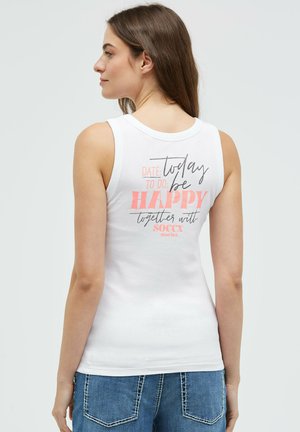 Young woman with brown hair in white sleeveless top with "Today be happy" text on back, wearing blue jeans, facing left.