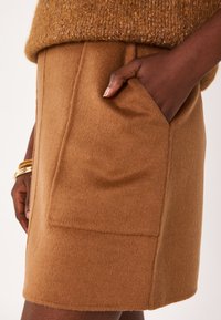 Jupe en laine marron avec une texture douce, poche latérale et design sur mesure. Présente des coutures visibles et une forme structurée.