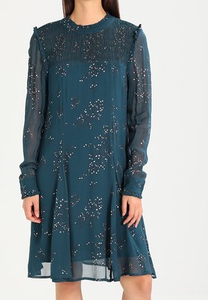 Türkisfarbenes Blumenmuster-Kleid mit transparenten langen Ärmeln, gerafftem hohem Kragen und Rüschendetails an Manschetten und Schultern, getragen von einer Person.