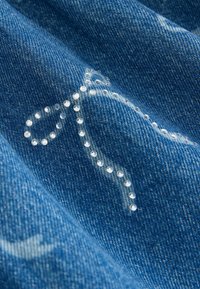 Jeansstoff mit einer glatten Textur. Verfügt über weiße Nähte und eine dekorative Spirale aus kleinen, glänzenden, klaren Strasssteinen.