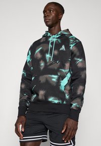 Sudadera con capucha en negro con un patrón de motas en turquesa y marrón. Cuenta con un bolsillo frontal y cordones turquesa. Textura de tela suave.