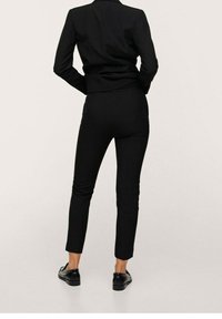 Veste de costume noire et pantalon ajusté vus de dos. Le tissu semble lisse avec une coupe sur mesure, et le pantalon présente une coupe fuselée.