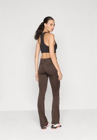 Top sportivo nero a croppato, leggings marroni a zampa d'elefante con cuciture laterali, tessuto morbido, stile atletico casual, scarpe da ginnastica a contrasto, design minimal.