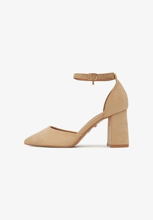 Sandalias de tacón alto de ante beige con puntera puntiaguda, correa en el tobillo y tacón grueso de bloque. Textura suave y detalles mínimos.