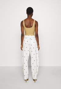 Bežový žebrovaný top na ramínka s širokými popruhy, kombinovaný s bílými kalhotami s širokými nohavicemi, které mají černé geometrické vzory a přední kapsy.