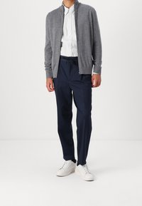 Šedá zipovací mikina, bílá pruhovaná košile, tmavě modré kalhoty a bílé tenisky. Měkká tkanina, casual design, elastický pas a viditelné švy.