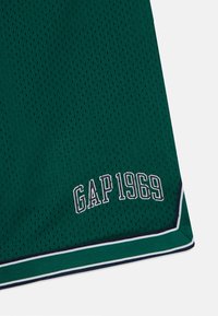 Zöld hálós sportshort, amelyen fehér hímezéssel található a "GAP 1969" felirat, kontrasztos sötétkék és fehér csíkkal díszített szegéllyel.