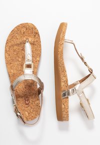 Korkkisaappaat, joissa on metalliset kultanauhat. Littee muotoilu, jossa on teksturoitu sisäpohja ja säädettävä solki. Vaalea ruskea kumipohja.