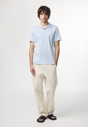 Lyseblå kortærmet polo-shirt parret med cremfargede, strukturerede brede bukser og sorte slidersandaler. Enkel, afslappet stil.