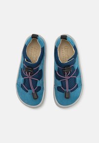 Siniset mokka- ja kangaskengät, joissa on teksturoitu muotoilu, joustavat nauhat ja kumipohja. Varustettu nyörein sulkijalla ja harmailla yksityiskohdilla.