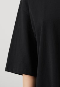 T-shirt en coton noir avec une coupe ample, des manches courtes et une texture lisse. L'ourlet est droit, sans motifs ni accents visibles.