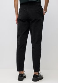 Pantaloni neri tapered con una finitura in tessuto liscia, caratterizzati da un dettaglio della tasca posteriore e una cintura elasticizzata per il massimo comfort.