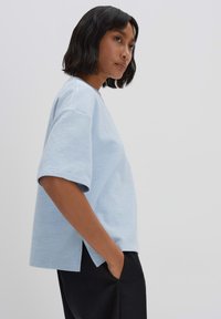 lichtblauw kortemouwen top met een textuurafwerking, voorzien van een losse pasvorm en zijsplitten, gecombineerd met zwarte broek.