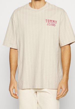 Beige gestreept t-shirt van zacht katoen met een ronde hals. Voorzien van een rood "TOMMY JEANS" logo op de linkerborst. Losvallende mouwen.