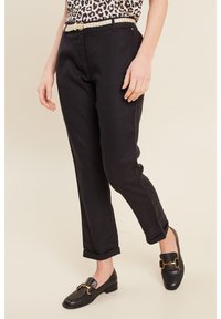 Zwarte linnenbroek met een omgeslagen zoom, gecombineerd met een top met luipaardprint en zwarte instappers met gouden hardware accenten.