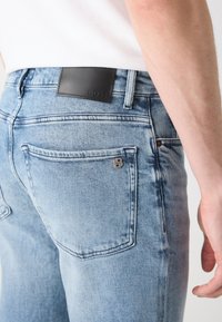 Lys blå denim jeans med slim fit, med et svart lærmerke merket "BOSS," og et metalllogo-akkent nær baklommen.