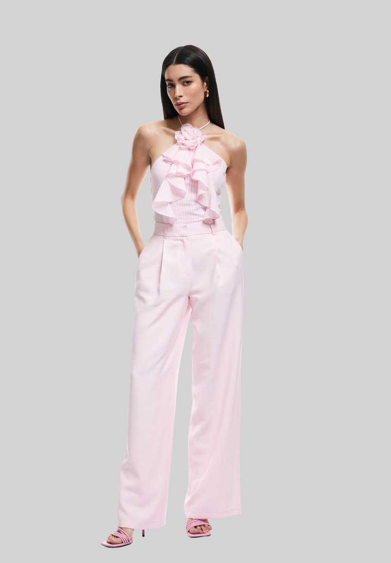 Rosa, volangig halterneck-top med blommaccent, matchande med skräddarsydda, högmidjade rosa byxor. Modellen bär matchande rosa klackar med remmar.