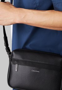 Borsa a tracolla nera in pelle con superficie strutturata, design elegante, tracolla regolabile e finiture in argento con il logo Calvin Klein.