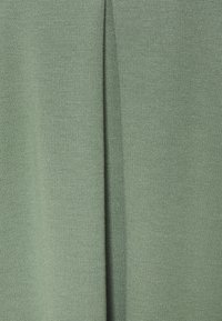 Tessuto texturizzato in un verde morbido e tenue, con una cucitura verticale centrale. Il materiale sembra leggero e traspirante, con un delicato motivo di intreccio.