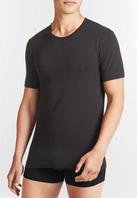 T-shirt nera a maniche corte in morbido cotone, con scollatura rotonda e superficie liscia, abbinata a pantaloni corti neri aderenti.